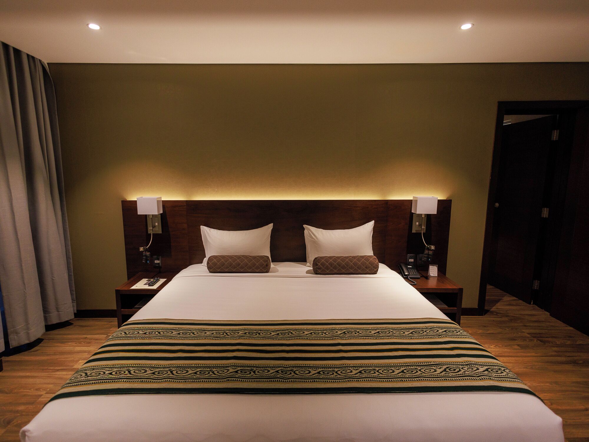 Une chambre d’hôtel avec un grand lit, deux tables de chevet, une tête de lit dotée d’un éclairage intégré et un plancher en bois.