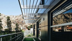A corridor with a green artificial turf, metal railings, and large windows offering a view of a mountainous town. - Hotel Rennova (La Paz)