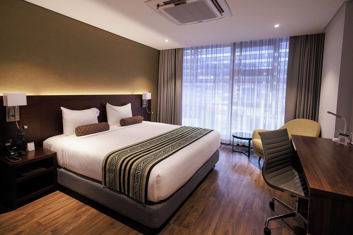 A hotel room with a large bed, a desk, a chair, and a window with curtains.