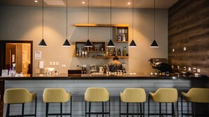 A bar area with a counter, multiple hanging pendant lights, and a wooden shelf with bottles. There are five yellow bar stools in front of the counter. - Hotel Rennova (La Paz)