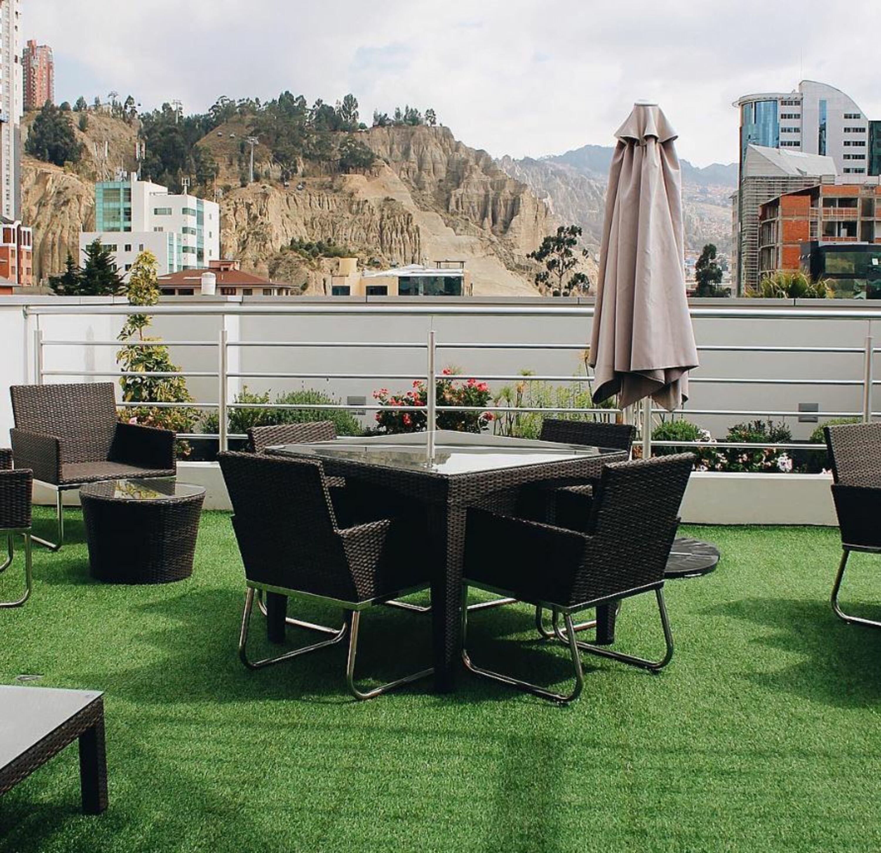 Un patio al aire libre con una mesa y sillas, rodeado de follaje y vistas a un paisaje montañoso.
