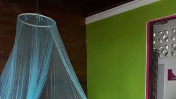 A room with a bed under a mosquito net, a green wall, a tiled floor, and a toilet visible through a door.