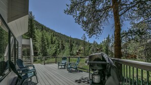 A wooden deck with outdoor seating and a grill, surrounded by a forested hillside. - Keystone Bristlecone Home 31 (Keystone)