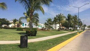 A street with a sidewalk, palm trees, and buildings in the background.