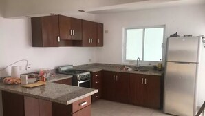 A modern kitchen with wooden cabinets, a stainless steel refrigerator, a gas stove, and a window providing natural light.