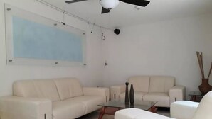 A modern living room with a beige sofa, a glass coffee table, and a ceiling fan. - Casa Pinos V (Mazatlán)
