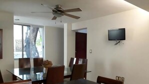 A dining area with a glass table, chairs, a ceiling fan, and a TV mounted on the wall. - Casa Pinos V (Mazatlán)