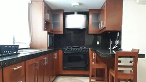A kitchen with wooden cabinets, a black stove, a sink, and a chair. - Casa Pinos V (Mazatlán)