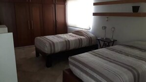 A bedroom with two beds, a wardrobe, a small table, and a window. - Casa Pinos V (Mazatlán)