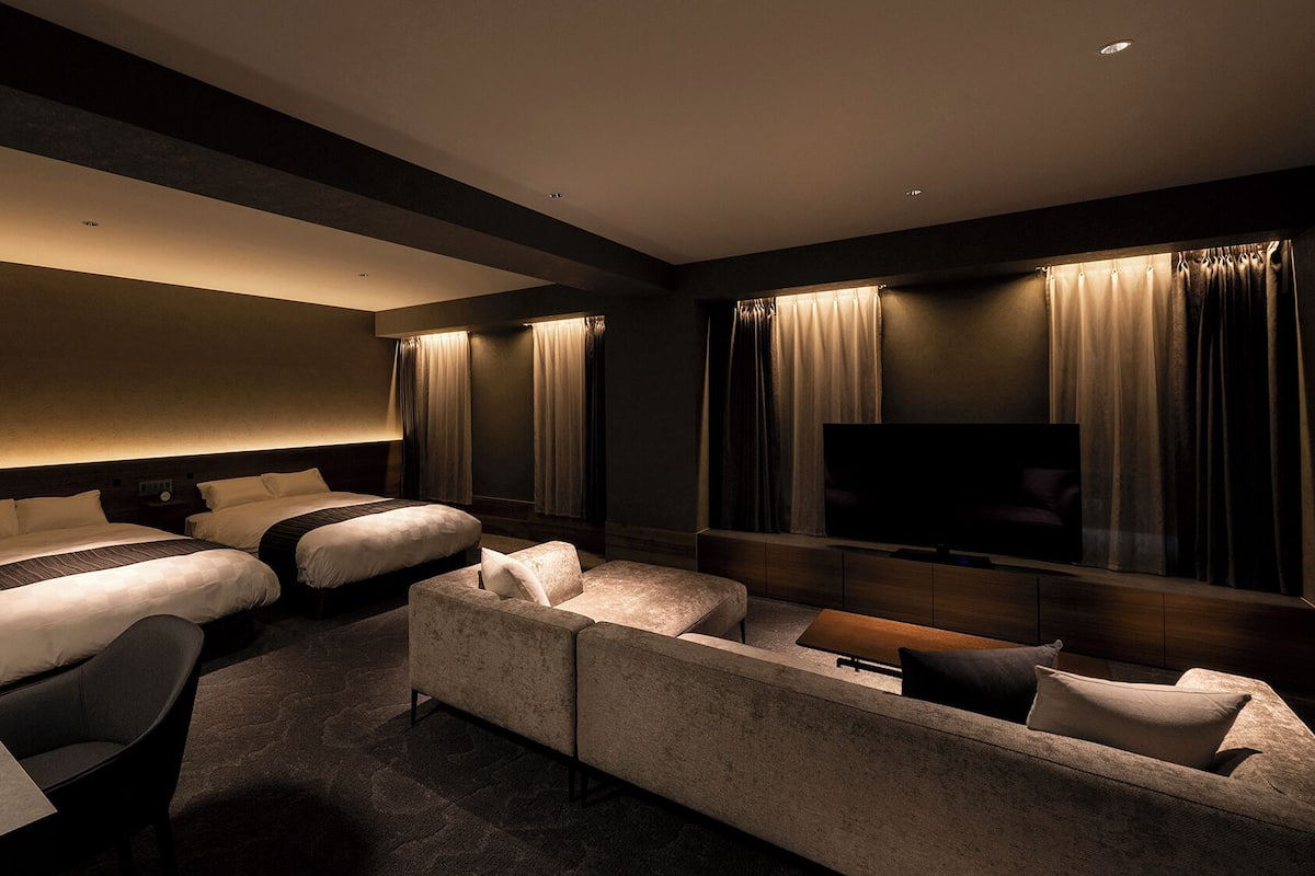 A hotel room with two beds, a sofa, a TV, and a desk.
