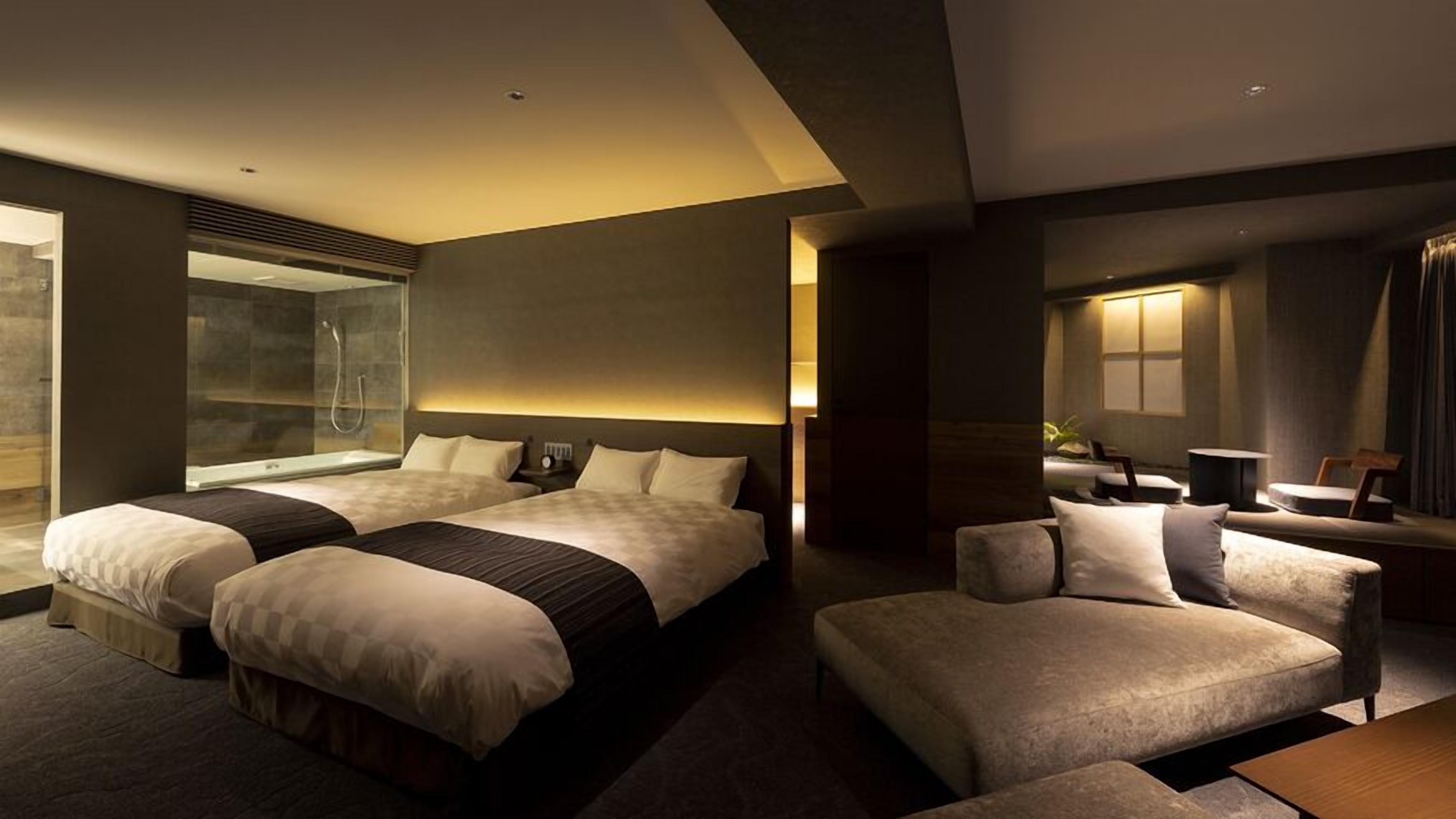Une chambre d’hôtel moderne avec deux lits, un coin salon, une douche et une grande fenêtre.