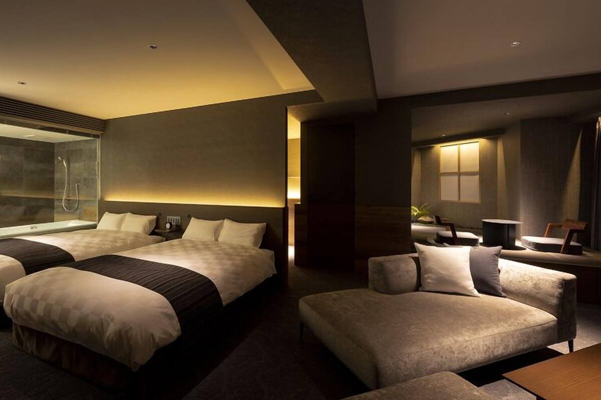 A modern hotel room with two beds, a seating area, a shower, and a large window.