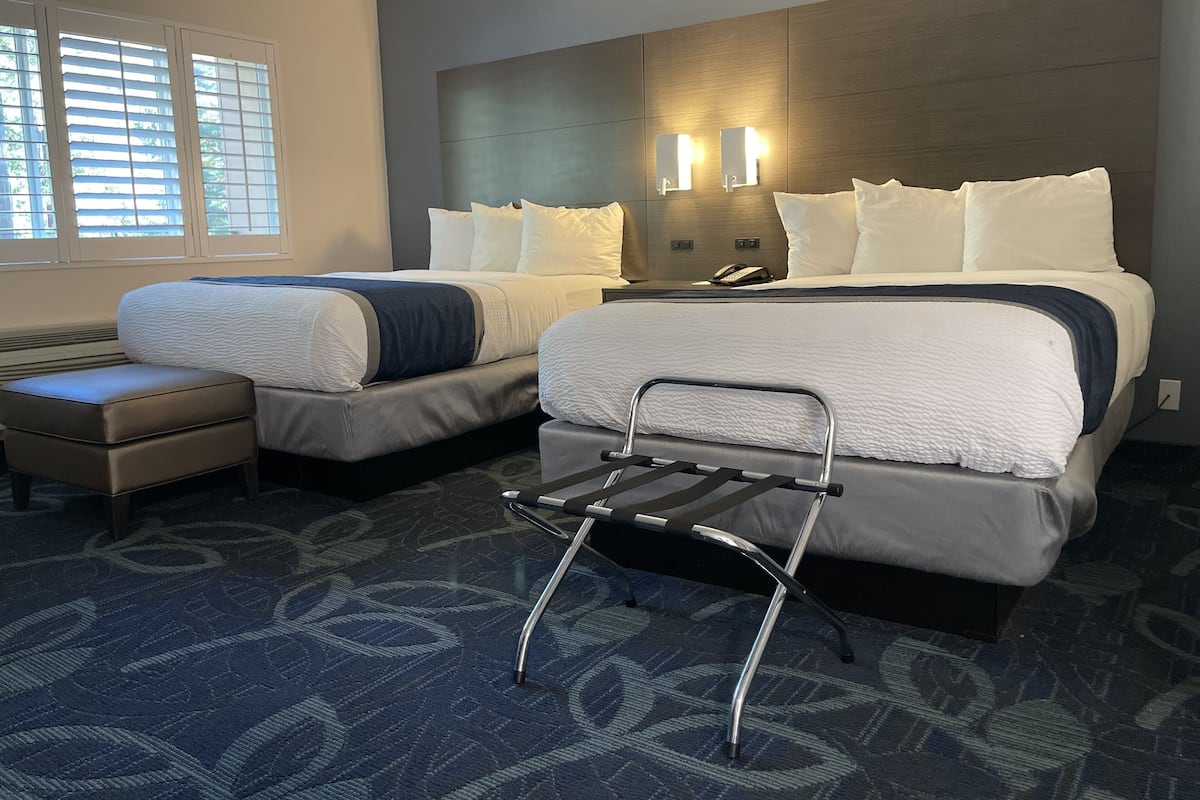 A hotel room with two beds, a small seating area, and a headboard with built-in lighting.