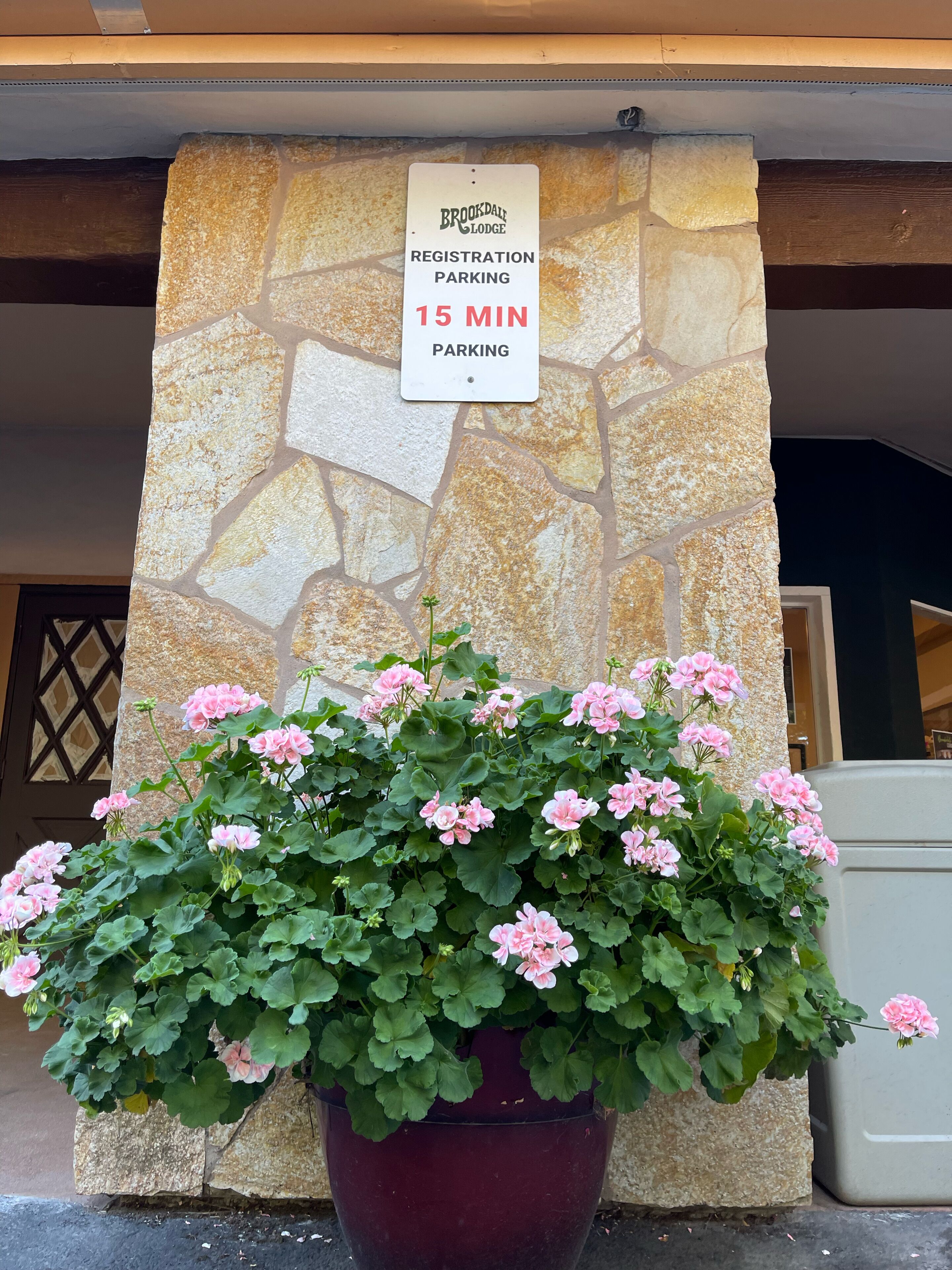 Muro de piedra con señal de estacionamiento para registro y una jardinera grande con flores rosadas.