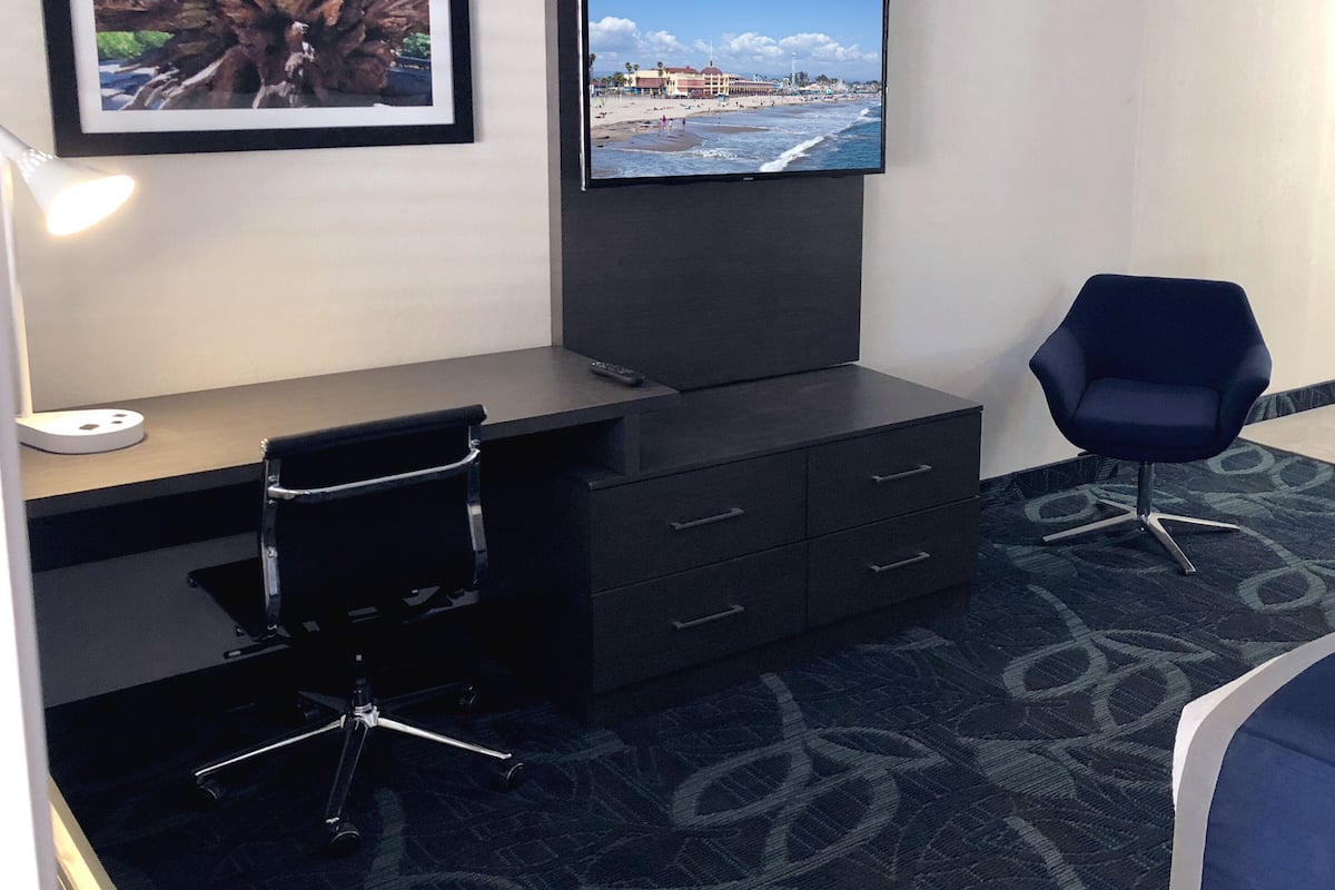 A hotel room with a desk, chair, TV, and a framed picture on the wall.