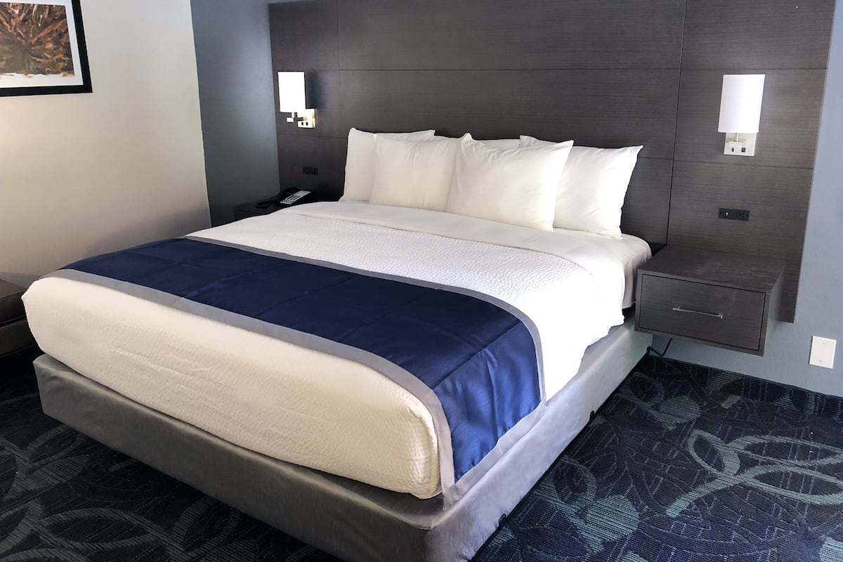 A hotel room with a large bed, a bedside table, a nightstand, and a wall-mounted light fixture.