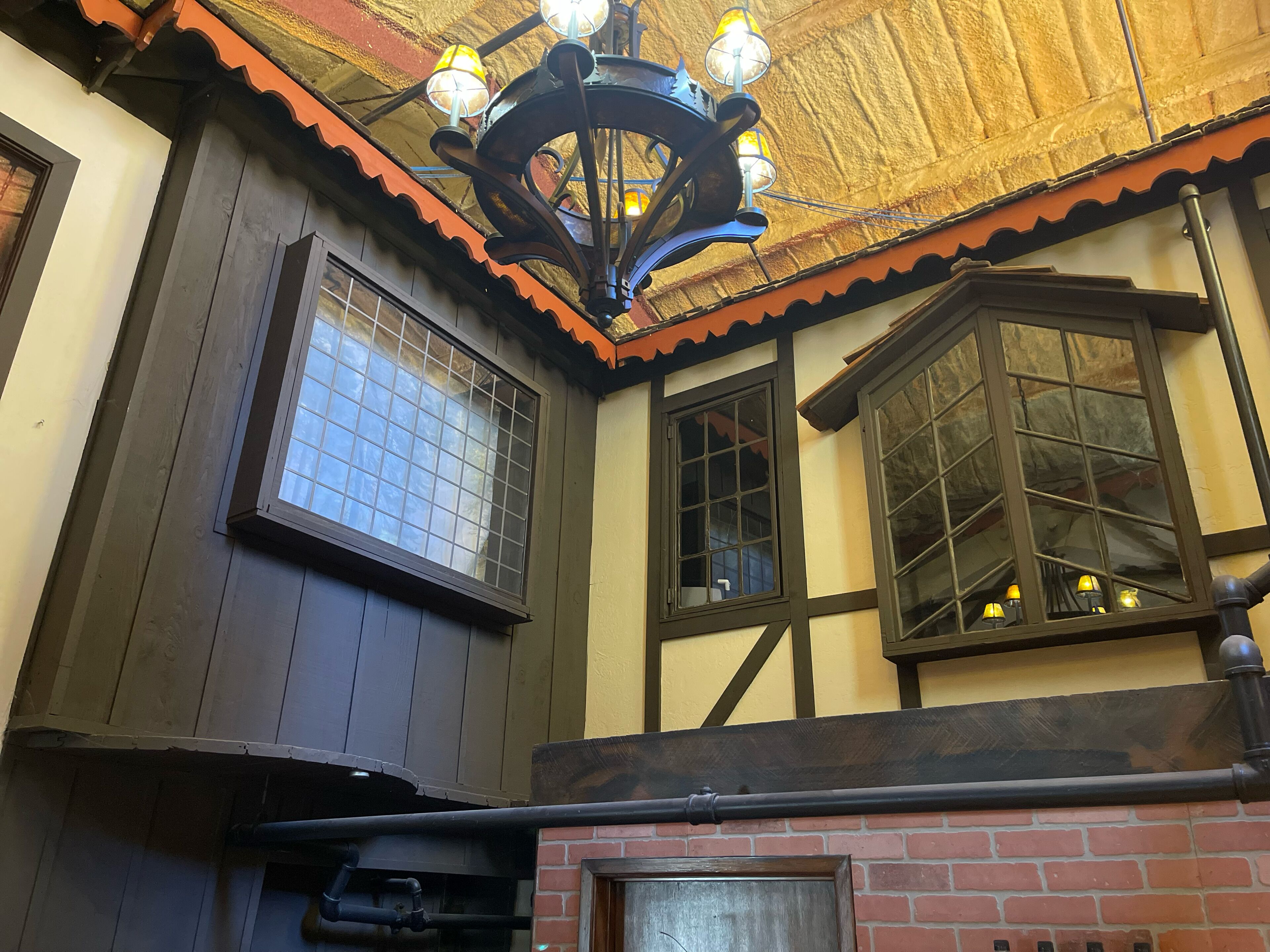 A room with wooden walls, a tiled floor, and a brick fireplace. There are multiple windows with wooden frames and a chandelier with multiple light fixtures.
