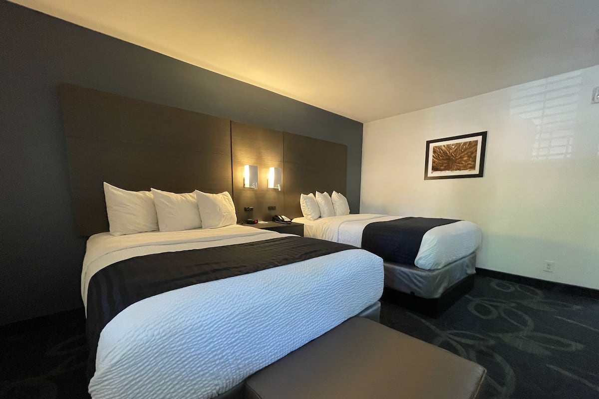 A hotel room with two beds, a bench, and a framed picture on the wall.