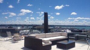 A rooftop terrace with outdoor seating, a view of the harbor, and a clear sky. - Heritage Apartment (Auckland)