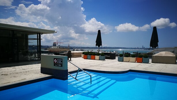 A rooftop pool with a clear view of the city skyline, a no running, no diving, no jumping sign, and a depth marker of 1.5m. - Heritage Apartment (Auckland)