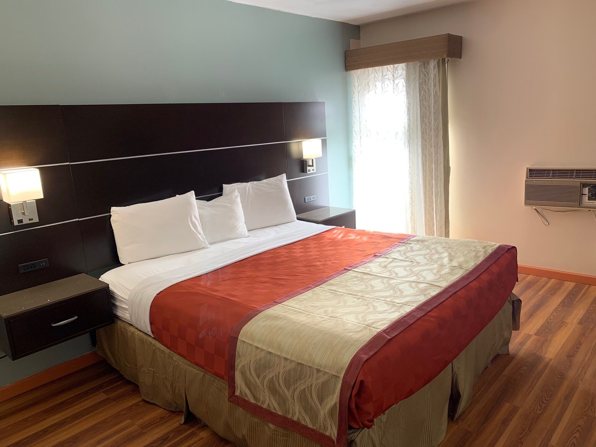 Een hotelkamer met een groot bed, een nachtkastje, een wandairconditioner en een raam met gordijnen.
