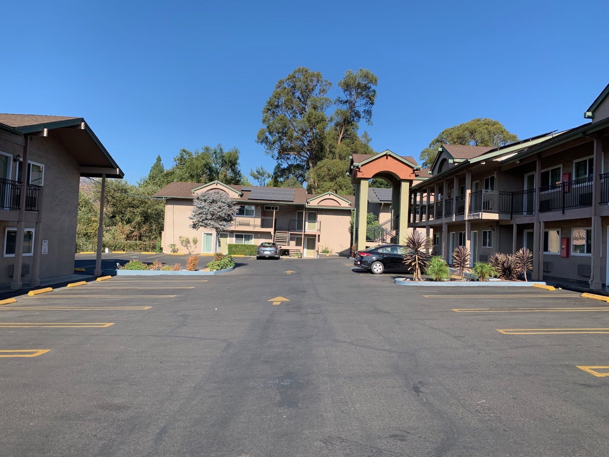A motel with a central entrance, multiple parking spaces, and a clear sky.