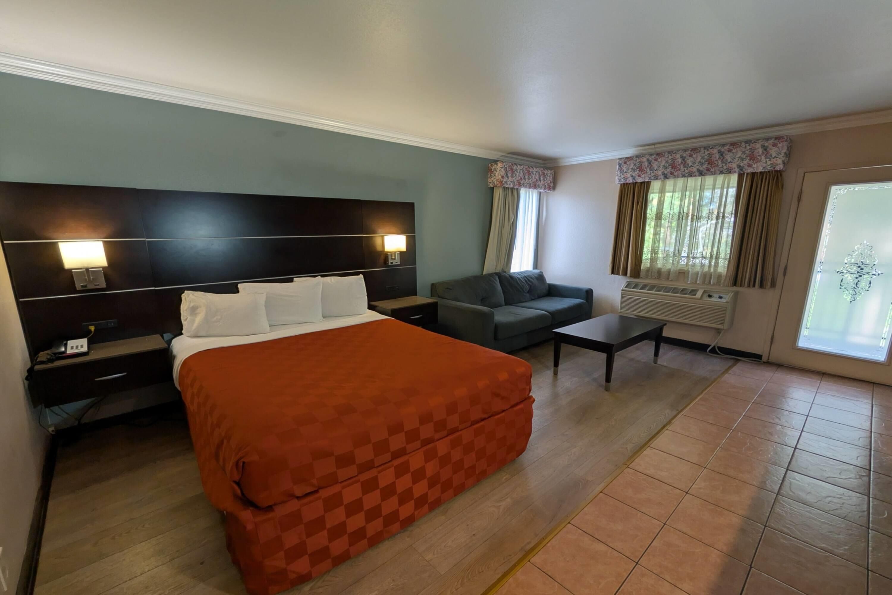 A hotel room with a bed, a sofa, a desk, and a window with curtains.