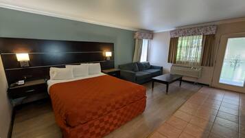 A hotel room with a bed, a sofa, a desk, and a window with curtains.