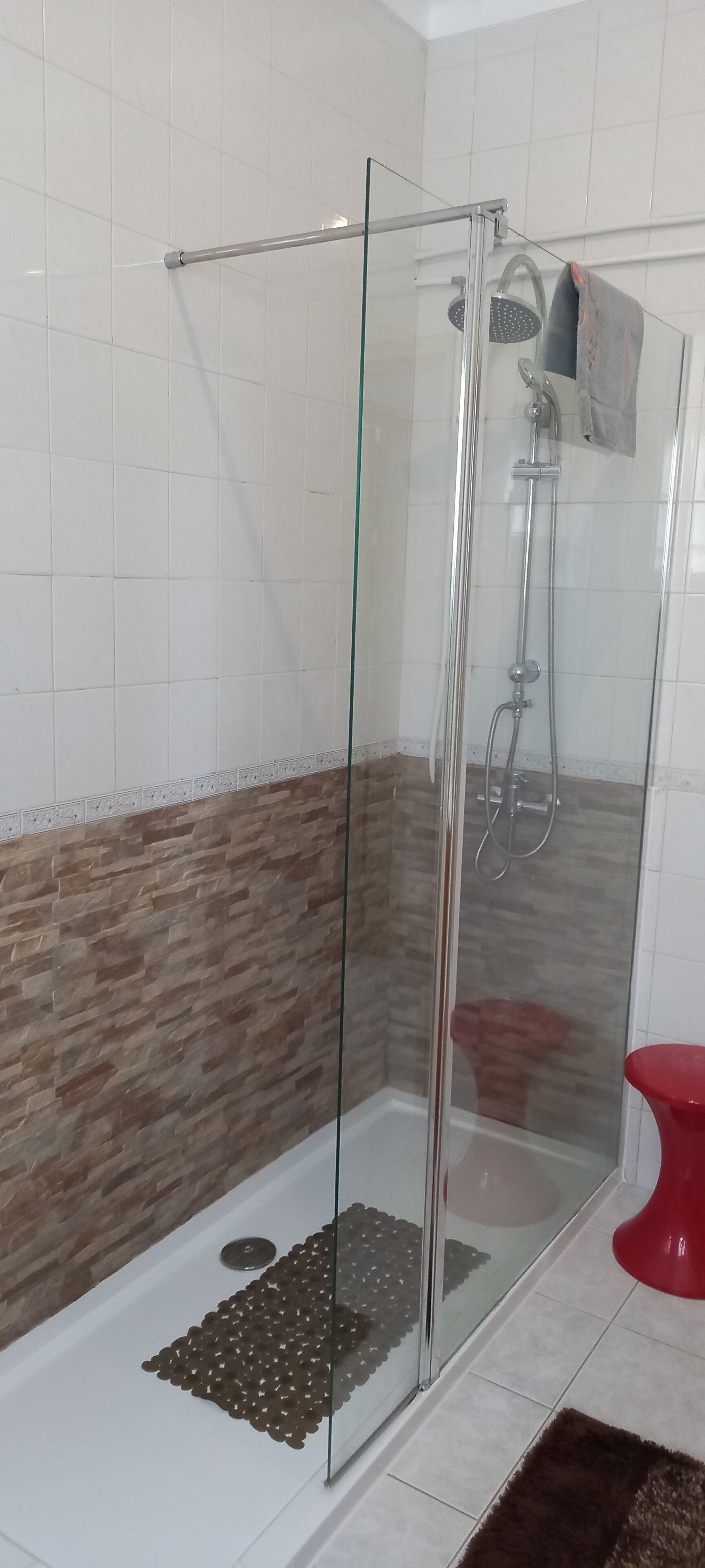 Une douche fermée par des parois en verre, dotée d’un pommeau de douche à main et d’un robinet mural.