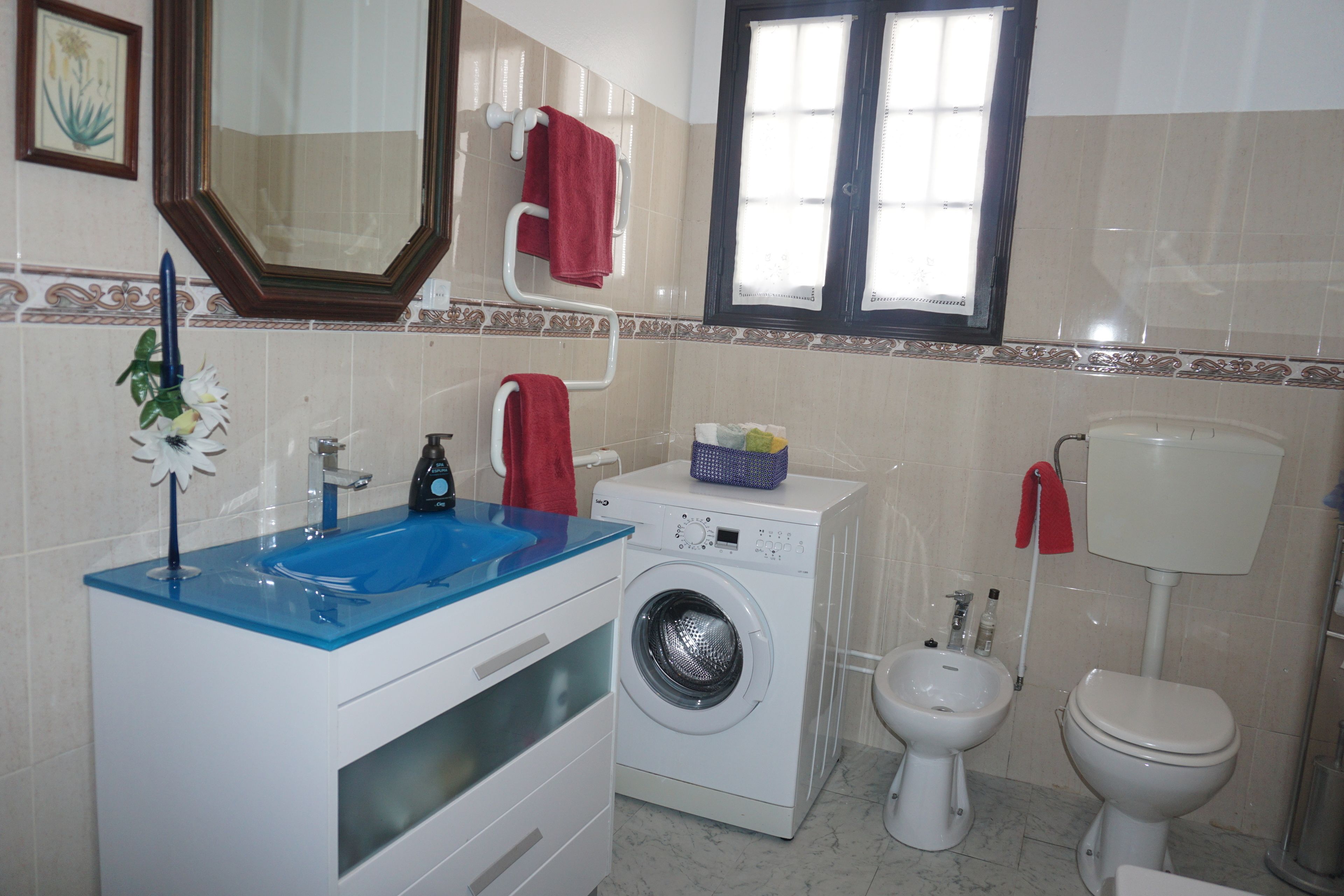 Een badkamer met een blauwe wastafel, een wasmachine, een douchetoilet en een toilet.