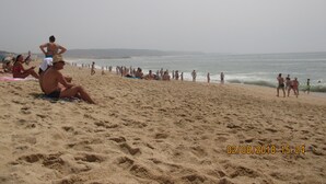 A crowded beach with people sunbathing and walking along the shore. - Casa Praia da Nazare (Nazaré)