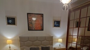 A bedroom with a large bed, two bedside tables with lamps, a headboard, and artwork on the walls. - Casa Praia da Nazare (Nazaré)