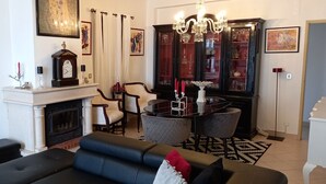 A living room with a fireplace, a chandelier, a dining table with chairs, and a television. - Casa Praia da Nazare (Nazaré)