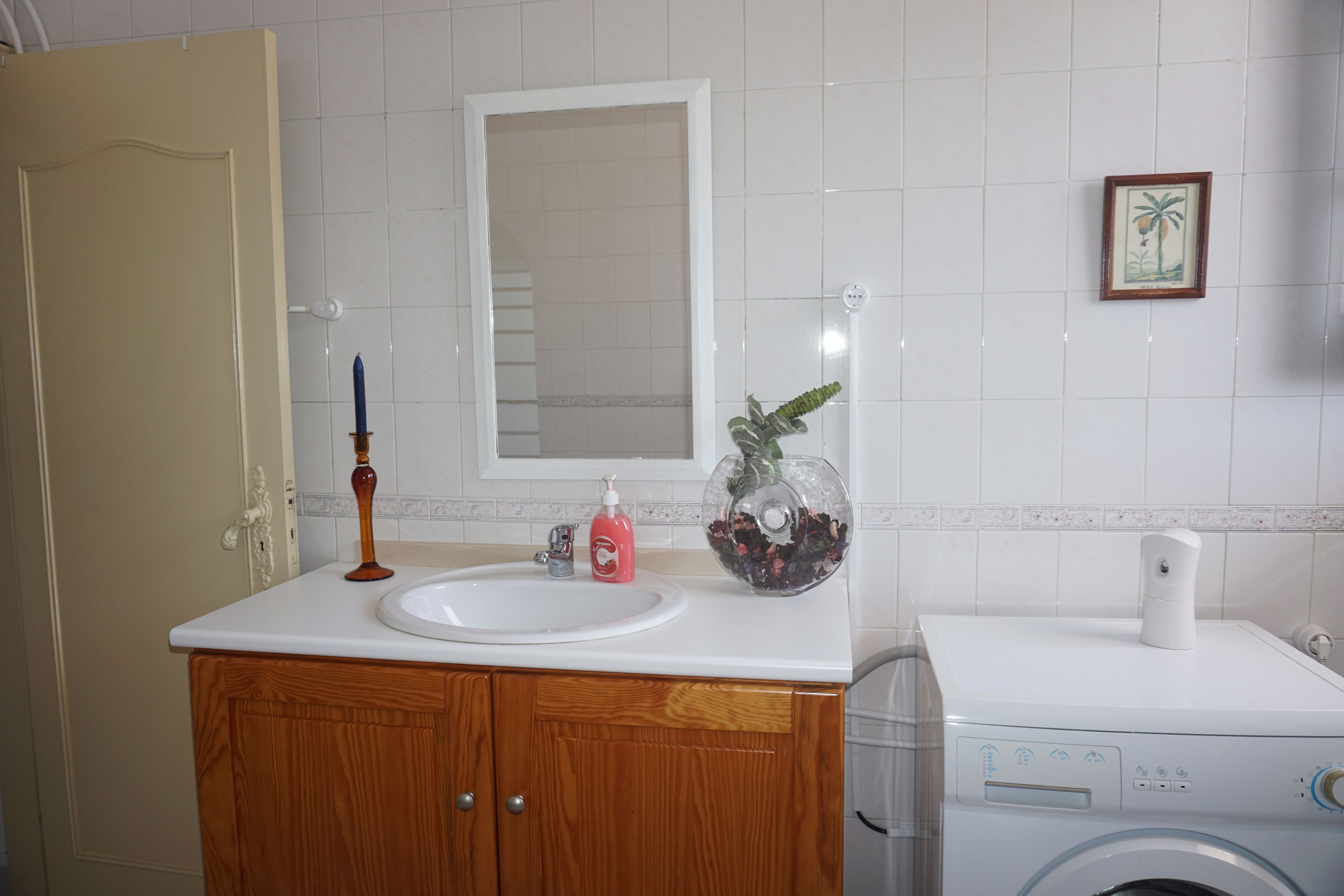Ein Badezimmer mit Waschtisch aus Holz, einer weißen Spüle, einem Spiegel, einem gerahmten Bild an der Wand und einer Waschmaschine.