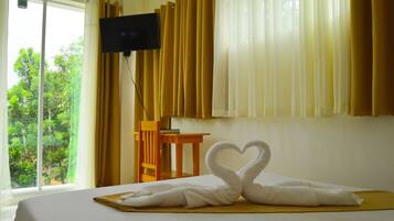 Habitación de hotel con cama, televisión montada en la pared, una silla de madera y ventana con cortinas.