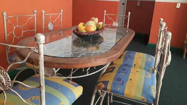 A dining table with a glass top and metal frame, surrounded by colorful cushioned chairs.