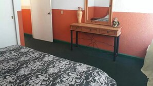 A room with a bed, a dresser with a mirror, and a door.