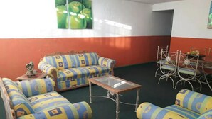 A living room with patterned sofas, a glass coffee table, and a dining area with metal chairs.