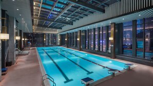 Una piscina interior con carriles delimitados, tragaluz y vista a la ciudad de noche.