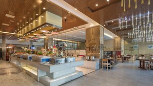Un amplio vestíbulo de hotel con una barra central, espacios para sentarse y un moderno candelabro.
