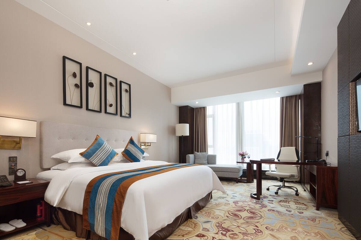 Quarto de hotel com uma cama grande, mesas de cabeceira, uma escrivaninha e uma cadeira.