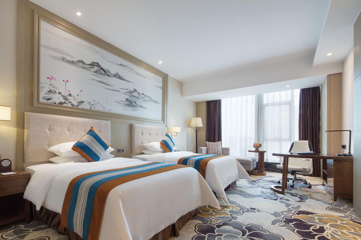 Quarto de hotel com duas camas, uma escrivaninha, uma cadeira e um quadro grande na parede.