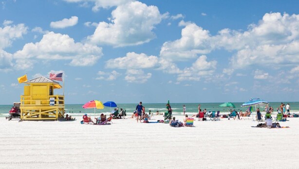 A beach with a lifeguard tower, umbrellas, and people relaxing on the sand. - Tropical Waterview Mansion (Sarasota)