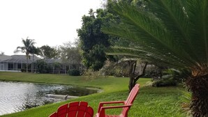 Two red chairs by a pond with a house in the background. - Tropical Waterview Mansion (Sarasota)