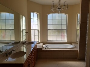A spacious bathroom with a large vanity, a freestanding bathtub, and three large windows providing natural light.