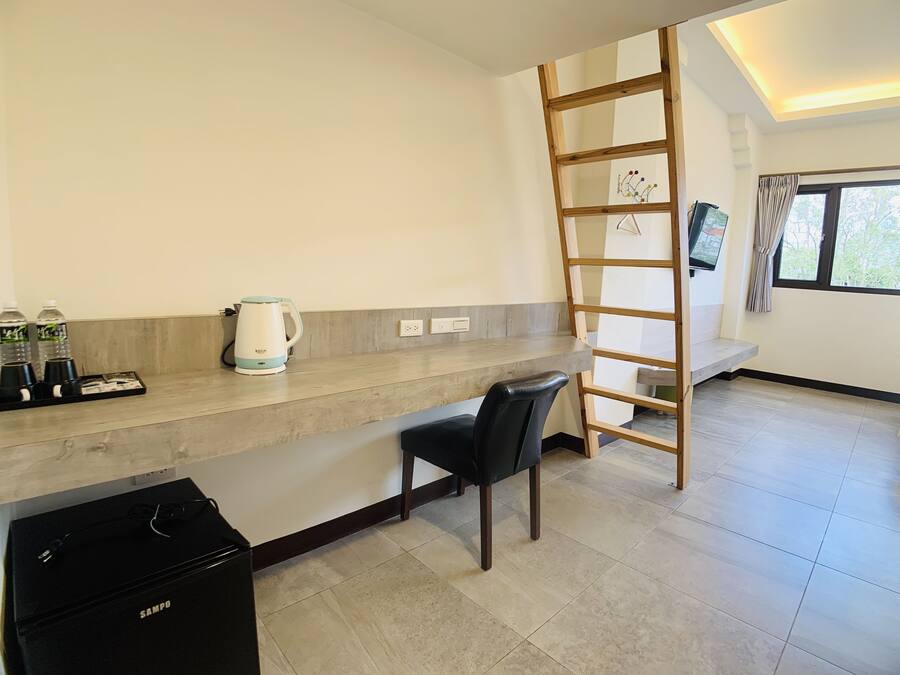 A modern kitchen with a built-in stove, a kettle, and a coffee maker. There is a wooden ladder leaning against the wall and a black trash bin.