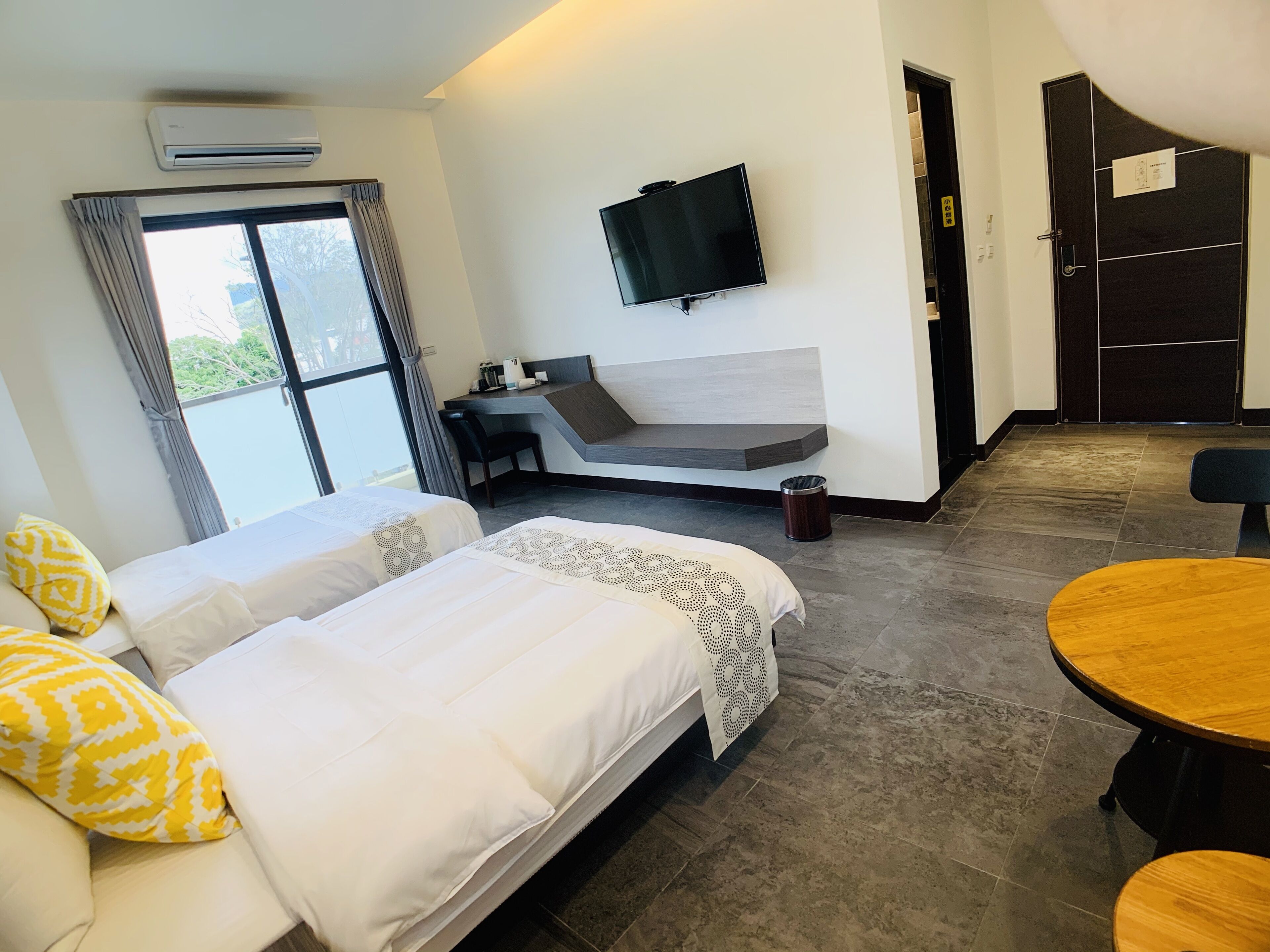 A hotel room with two beds, a desk, a TV, and a dining area.