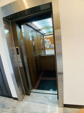 An elevator interior with a wooden finish, a control panel, and a bulletin board with notices. - Xuyu B&B (Chishang)