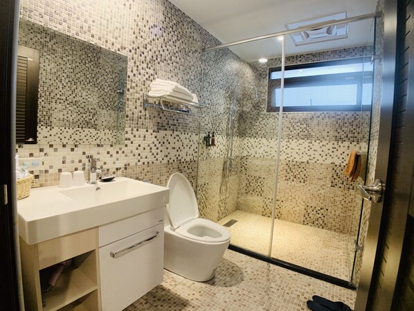 A modern bathroom with a glass-enclosed shower, a white sink, and a tiled mosaic wall.