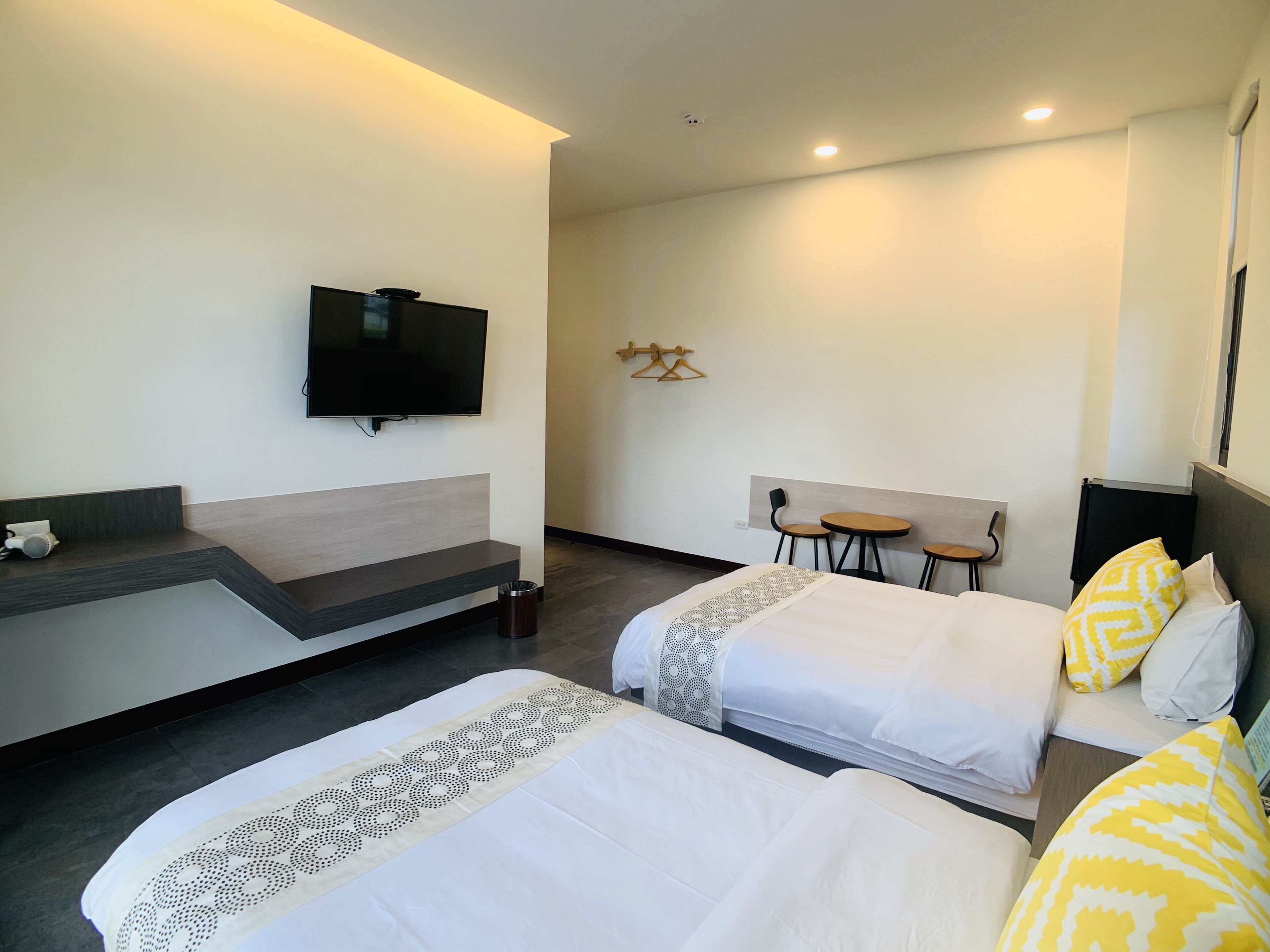 A hotel room with two beds, a TV mounted on the wall, a small table, and a chair.